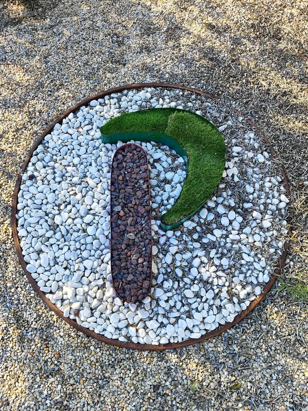 El símbolo de Perlovín construido en piedra: la P en grava granate y musgo verde